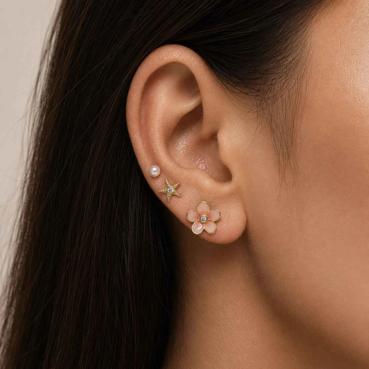 Gold starfish and flower drop earrings on ear, pearl studs with pink center