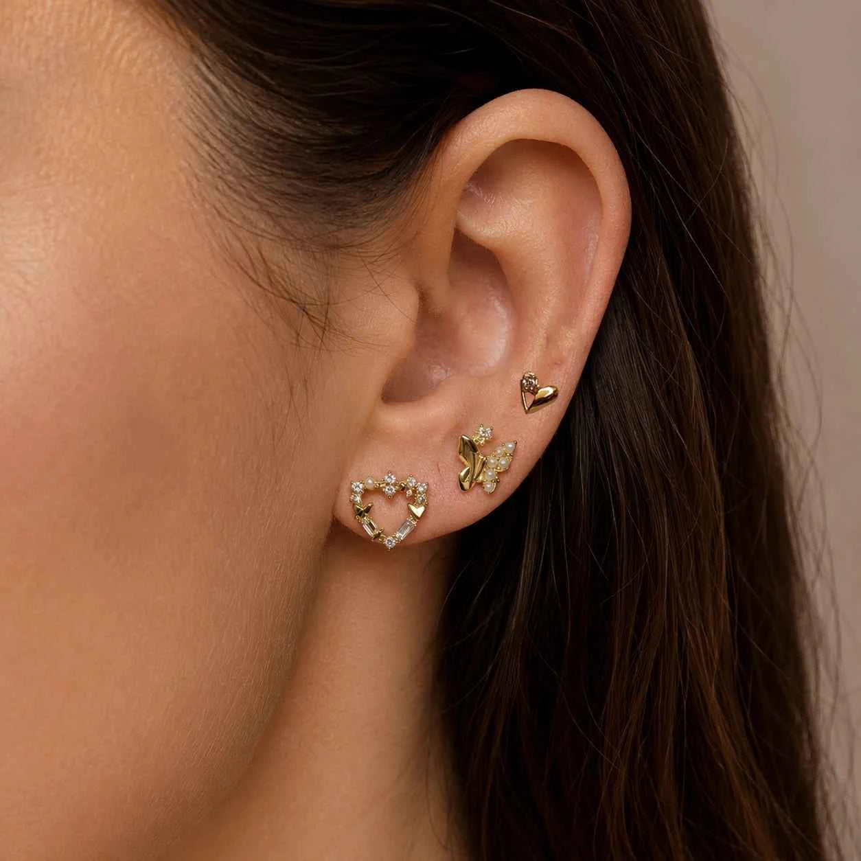 Gold-tone heart and butterfly stud earrings on ear