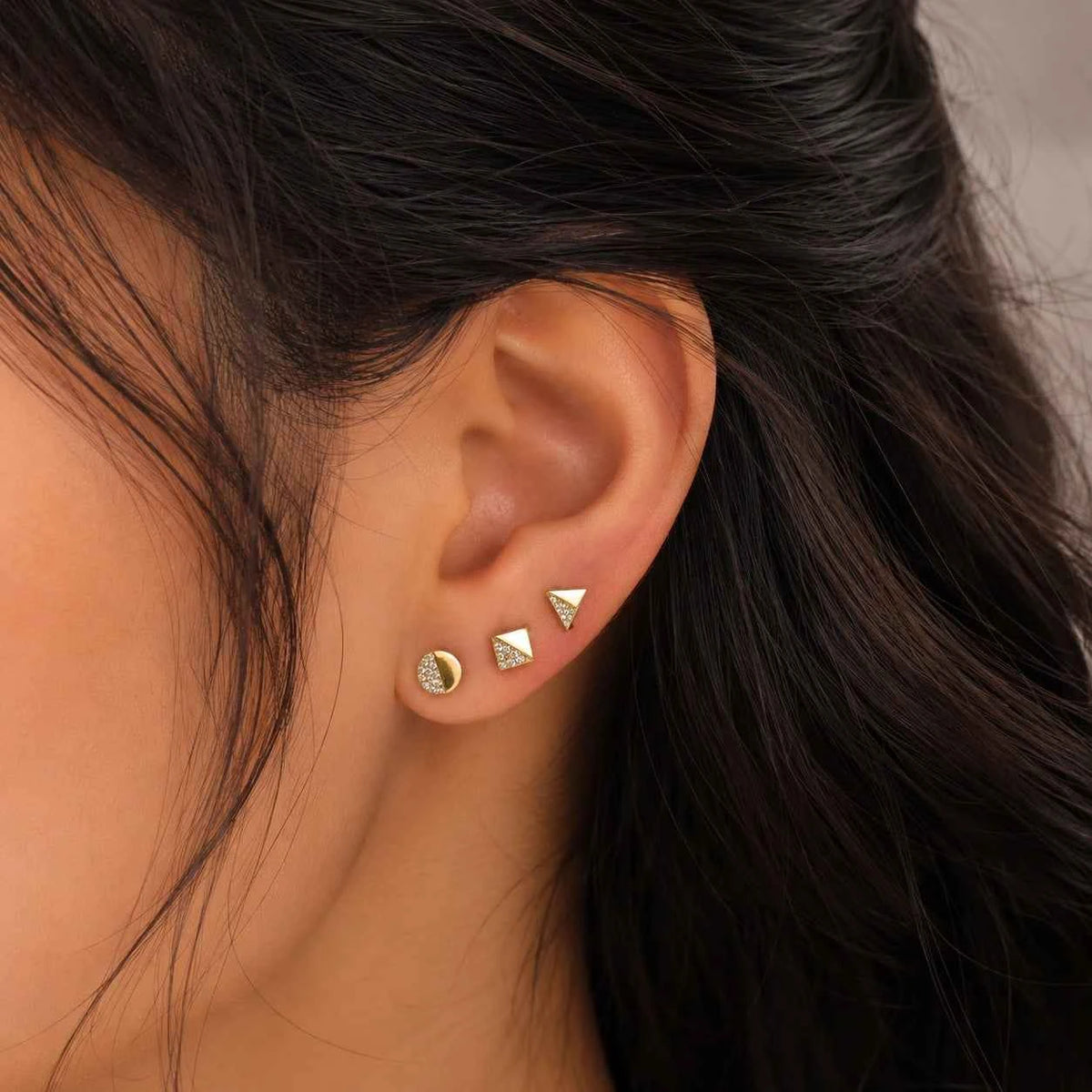 Triangular and circular stud earrings on ear, gold-tone small stacked set