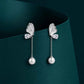 Butterfly-shaped earrings with pearl drops on a dark green background