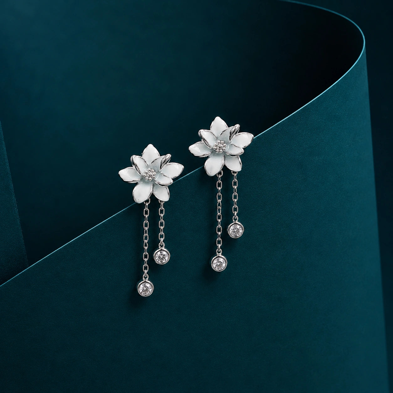 Silver flower-shaped earrings with dangling elements on a dark green background