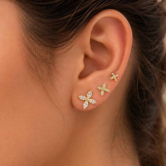 Gold four-petal floral side earrings worn on ear, stud and drop cluster