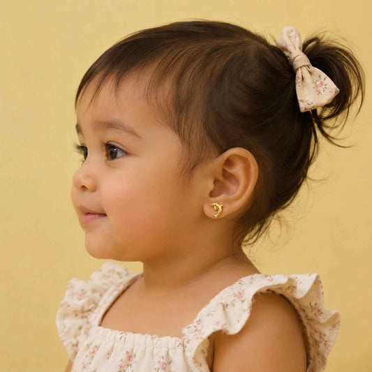 Small gold-tone dolphin stud earrings with clear stones, worn by a child