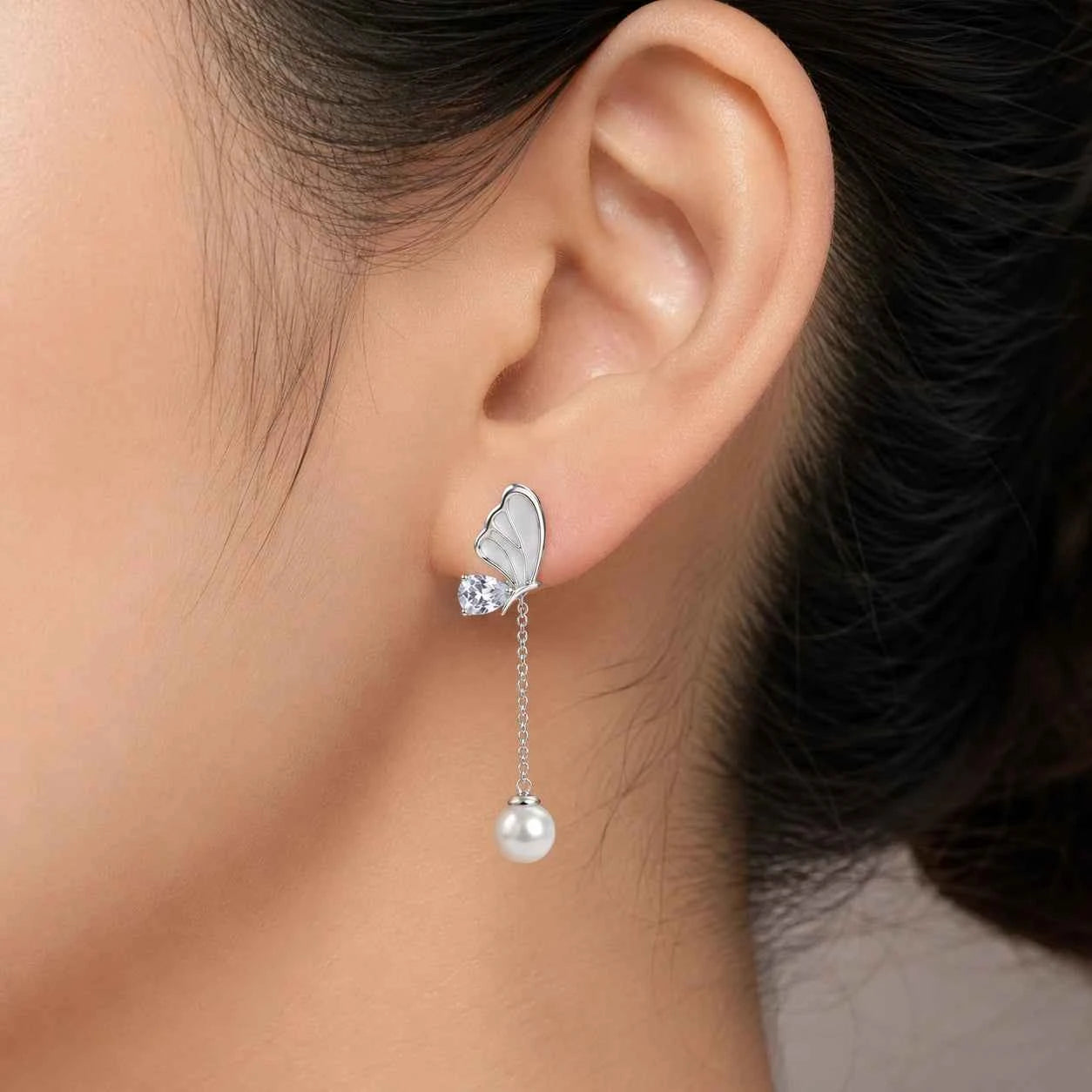 Silver butterfly earring with pearl drop worn by a person