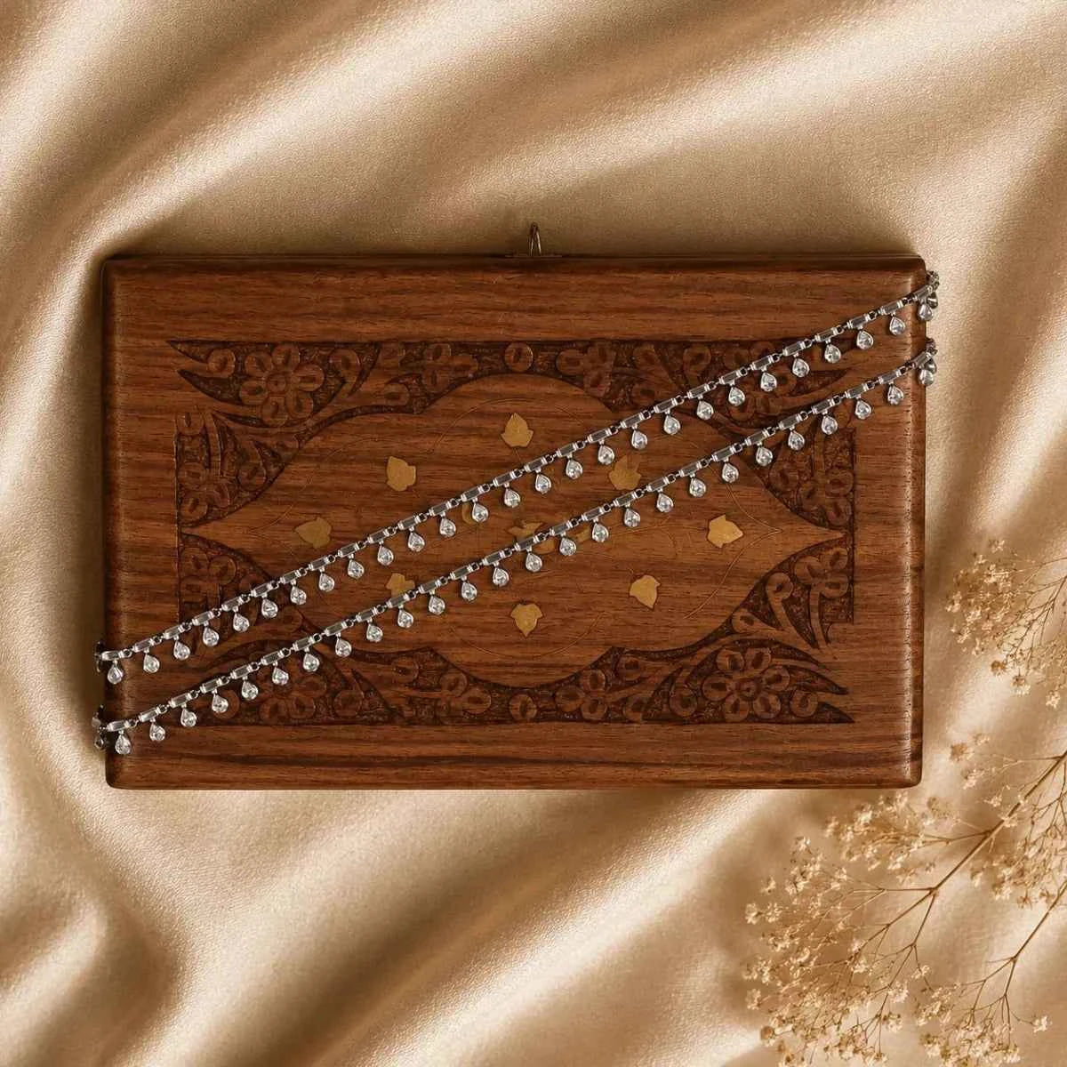 Silver crystal chain anklet draped across a wooden jewelry box