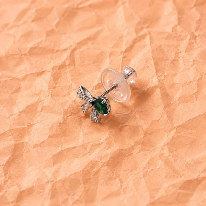 Silver bow charm stud earrings with emerald green gemstone centers, on posts.
