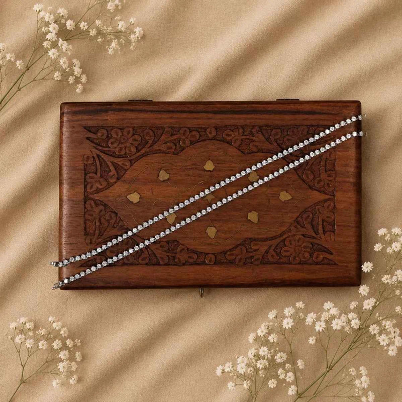 Silver 925 anklet pair with sparkling chain on wooden jewelry tray