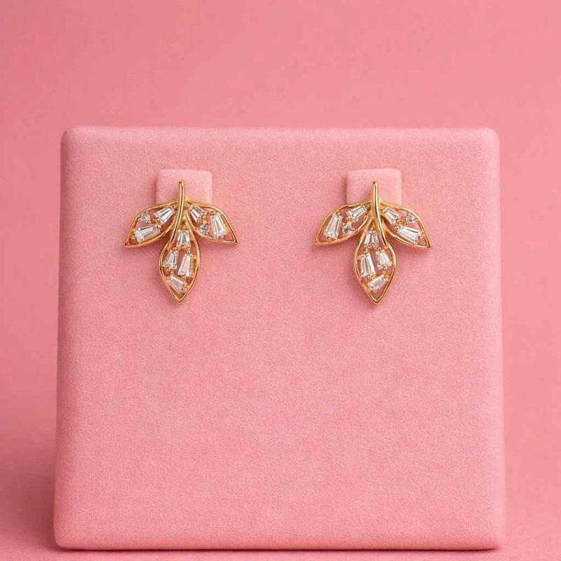 Gold-tone leaf stud earrings with clear baguette stones displayed on a pink stand