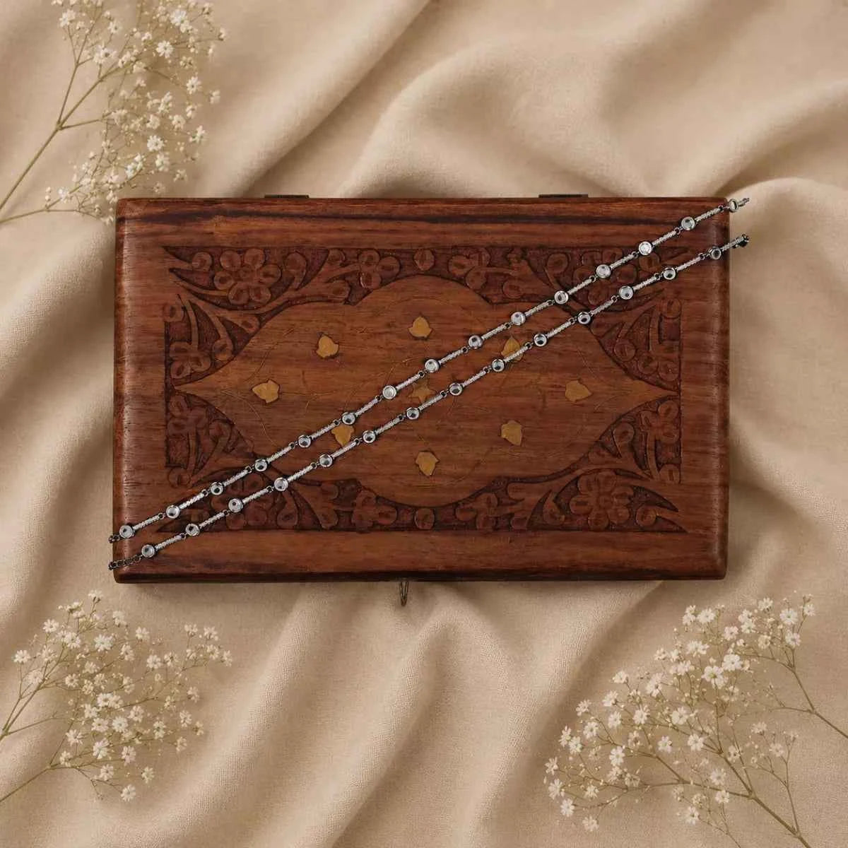 925 silver chain anklet with bead-like links, laid across a wooden box