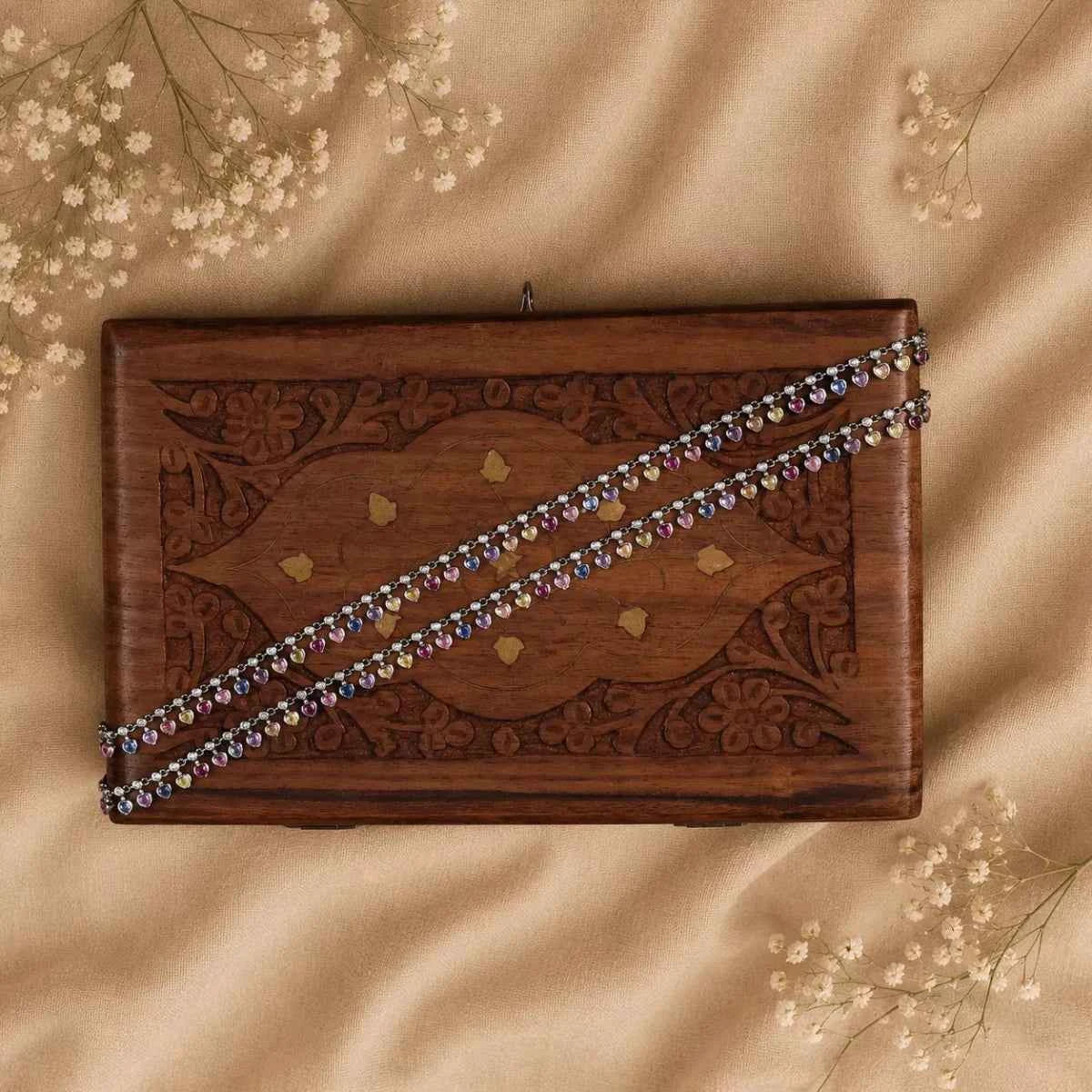 925 silver beaded anklet pair with small charms, laid diagonally on wooden box