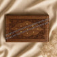 Silver chain anklet laid across a wooden box with decorative carvings